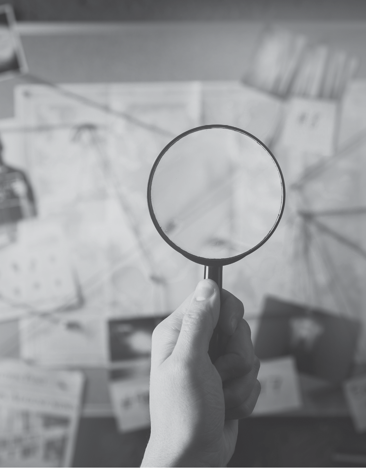 Detective hand holding a magnifying glass in front of a board with evidence, crime scene photos and map  high contrast image