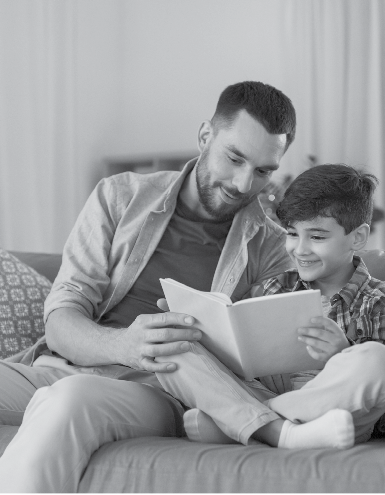 family, childhood, fatherhood, leisure and people concept - happy smiling father and little son reading book on sofa at home
